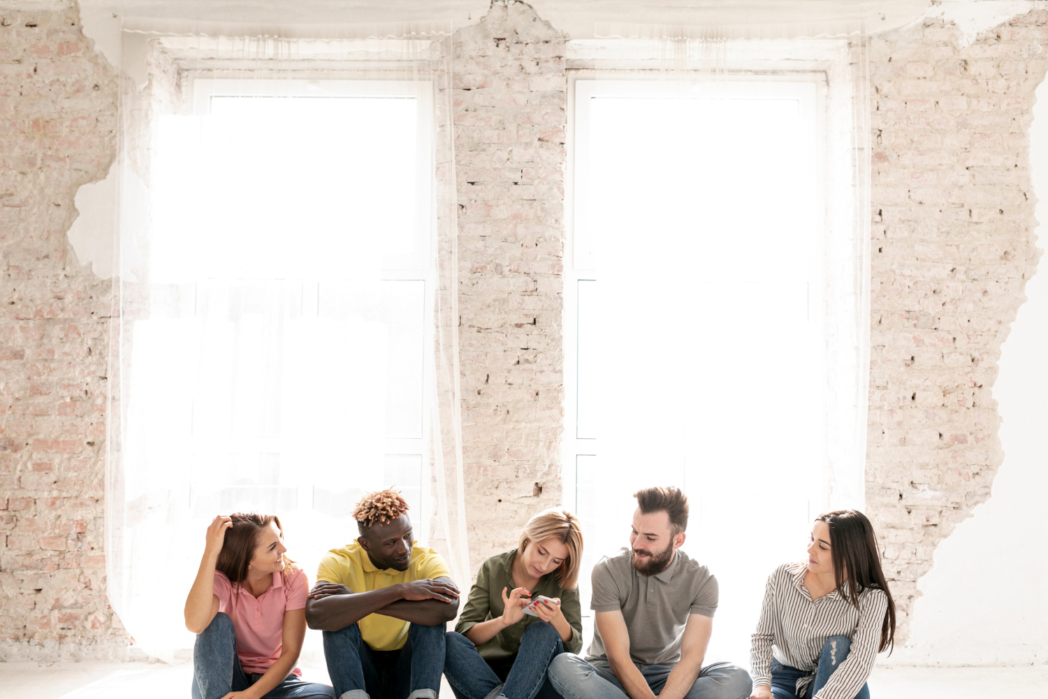 Five people sitting together on the floor in a bright, minimally decorated room.